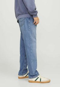 Helle blaue Denim-Jeans mit lockerer Passform, geraden Beinen und klassischem Fünf-Taschen-Design. Getragen mit weißen und grünen Turnschuhen.