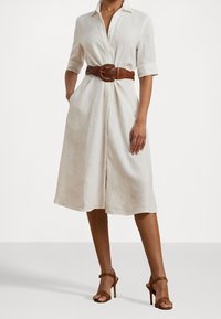 White linen shirt dress with short sleeves, featuring a front button closure, side pockets, and a wide braided brown leather belt.