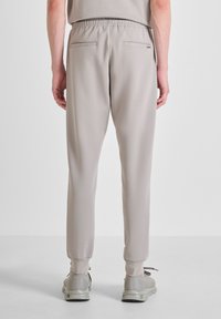 Pantalones de chándal beige claro con cintura ajustable, pierna ceñida y dos bolsillos traseros. Tejido suave con un ligero brillo.