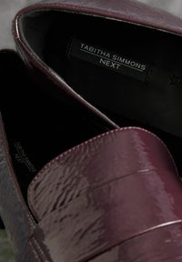 Burgundy patent leather loafers with a smooth texture, thick strap across the front, and black interior lining. Label reads "Tabitha Simmons NEXT."