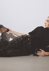 Gonna nera con paillettes e una texture trasparente, abbinata a una maglietta nera aderente e scarpe nere. Una pochette nera è visibile accanto alla mano.