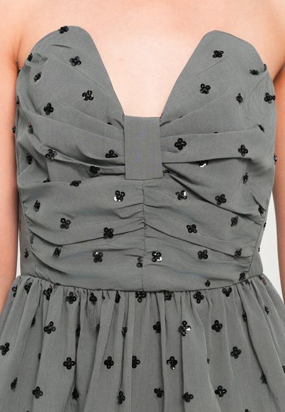 Γκρι φόρεμα με βαθύ ντεκολτέ, συγκεντρωμένη υφή και διακοσμημένο με μαύρα λουλούδια. Διαθέτει εφαρμοστό μπούστο και ρέουσα φούστα.