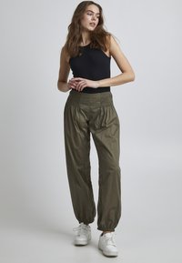 Pantalons élastiques de couleur olive avec ourlet froncé ; associés à un haut noir sans manches ajusté ; matière lisse et coupe décontractée.