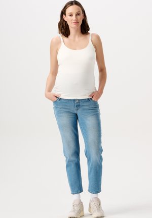 Witte tanktop met verstelbare bandjes, gecombineerd met lichtblauwe jeans met een slim fit. Model draagt beige sneakers met witte sokken.