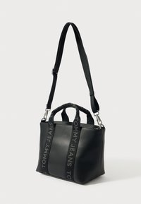 Mustast sünteetilisest materjalist käekott reguleeritava rihmaga, kahe ülemise sangaga, reljeefse logoga ja siledapinnaline. Kompaktse ruudukujuline disain.