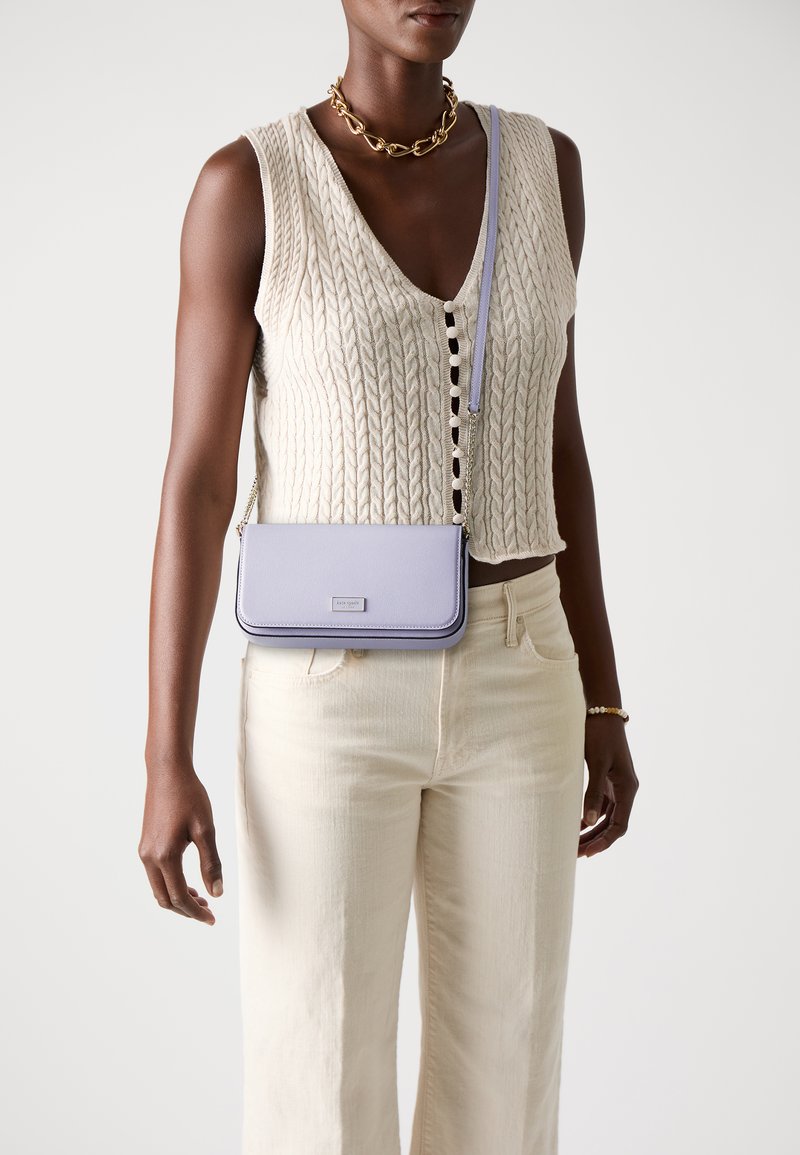 Light purple crossbody bag with smooth texture, rectangular shape, and chain strap. Worn with a cream knitted top and light beige pants.