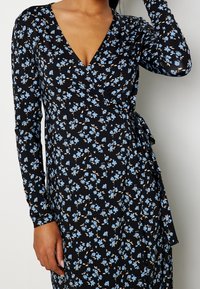 Černé květinové zavinovací šaty s dlouhými rukávy, ozdobené světle modrými květinami a vázáním v pase. Měkká, elastická látka s výstřihem do V.