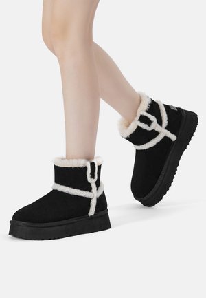 Schwarze Wildleder-Stiefeletten mit einem Futter aus Kunstfell und weißen Akzentriemen, ausgestattet mit einer dicken schwarzen Gummisohle und einem runden Zehen-Design.