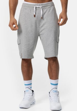 Shorts cargo en coton gris avec poches latérales, taille élastique et cordon blanc. Assortis avec des baskets blanches et des chaussettes rayées.