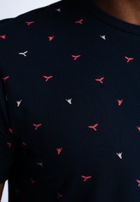 Námořnické tričko vyrobené z měkké tkaniny, s malými červenými a krémovými vzory připomínajícími ruce a ploutve po celém povrchu. Kulatý výstřih, krátké rukávy.