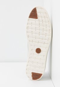 Semelle de chaussure en caoutchouc blanc cassé avec un motif texturé ; présente un accent marron au talon et un logo intégré au centre.