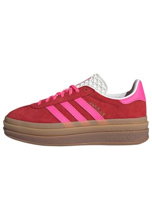Czerwony zamszowy sneaker z jaskrawymi różowymi paskami i sznurówkami, grubą warstwową brązową podeszwą oraz białym teksturowanym językiem.