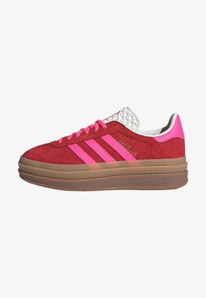 Baskets en daim rouge avec des bandes et lacets rose vif, semelle épaisse brune en couches, et languette blanche texturée.