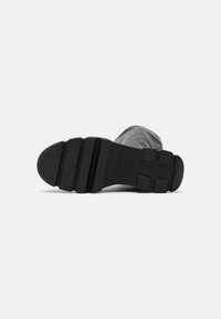 Semelle de botte en caoutchouc noir avec une surface striée, présentant des rainures horizontales et verticales. Logo estampé visible près du talon.