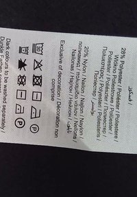 Étiquette d'entretien en tissu blanc avec texte noir, détaillant la composition du matériau (28 % polyester, 20 % nylon) et les instructions de lavage avec des symboles.