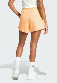 Calções de atletismo cor pêssego com cintura elástica, textura suave e bolsos laterais, combinados com meias brancas e ténis.