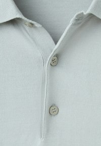 Gros plan sur un polo gris clair en tricot montrant le col et trois boutons beiges sur la patte de boutonnage.