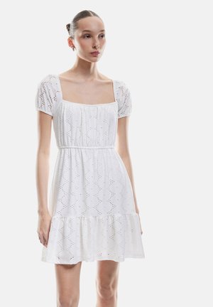 Vestido blanco con mangas cortas abullonadas, escote cuadrado y patrón de ojal bordado. Falda acampanada con dobladillo con volantes, tejido ligero.