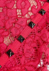 Röd spetstyg med ett blommönster, med ett texturerat svart nubbband som löper över designen.