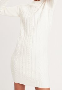 Abito maglione lavorato a maglia bianco con motivi a treccia testurizzati, collo alto e orlo a coste, maniche lunghe e una silhouette attillata.