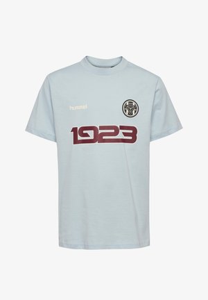 Jasnoniebieska koszulka z krótkim rękawem z "1923" w dużym ciemnoczerwonym nadruku, okrągłą czarno-białą emblematem oraz logo "hummel" na piersi.