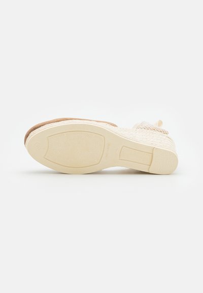 Suola di scarpa beige con fondo in gomma testurizzata, sezione superiore intessuta e tacco leggero. Presenta una punta arrotondata e accenti decorativi.