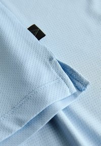 Gros plan sur un tissu bleu clair perforé avec une petite étiquette noire et une couture soignée avec une petite fente.