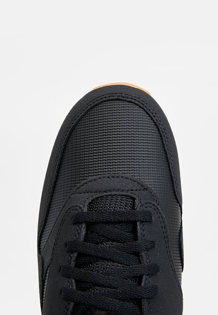 Zwarte sneaker met een gestructureerde bovenkant van stof, ronde neus en zes vetersleuven. Rubberen zool, gedetailleerde stiksels en subtiele ontwerpelementen.