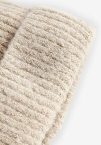 Tissu tricoté beige avec une texture douce et duveteuse et un motif en côtes. Gros plan montrant des détails fins et des éclats brun clair tout au long.
