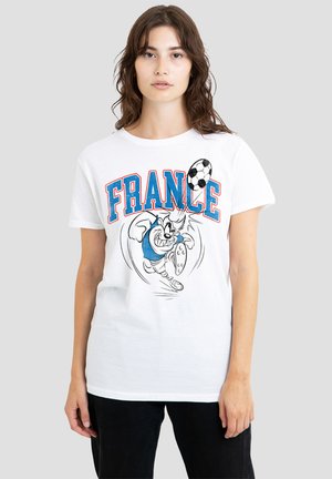 Junge Frau mit braunen Haaren trägt ein weißes T-Shirt mit dem Text "FRANCE" und einer Cartoonfigur, die einen Fußball kickt.