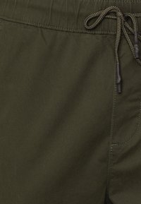 Olijfgroene korte broek met elastische tailleband en trekkoord, met een soepele textuur en een zijzak. De stof lijkt lichtgewicht en duurzaam te zijn.