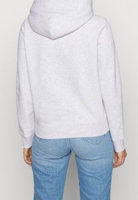 Felpa grigia chiara in cotone con tasca a marsupio, polsini e orlo a costine, caratterizzata da una texture morbida e un cappuccio con cordino regolabile.