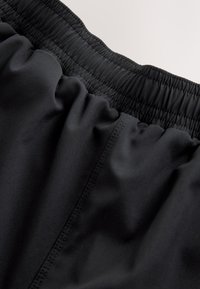 Gros plan sur la ceinture élastique noire et les plis du tissu sur un pantalon ou un short léger et ample.