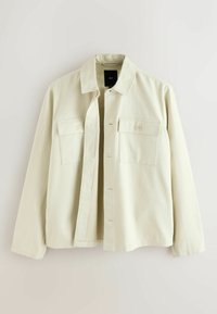 Veste boutonnée de couleur crème avec deux poches poitrine à boutons et un col, présentée sur un fond clair.