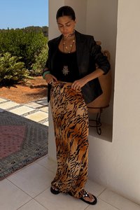 Gonna lunga e fluida con stampa tigre in marrone e nero, realizzata in tessuto leggero. Indossata con un top nero e gioielli a strati.