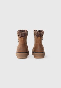 Bottines en cuir marron avec un poignet en tricot texturé, fermeture éclair latérale et talon empilable, présentant une pointe ronde et des accents décoratifs minimaux.