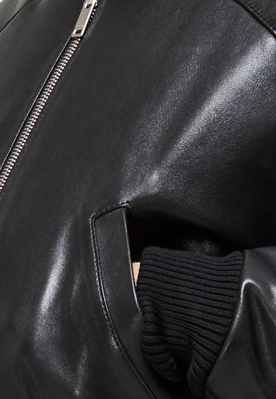 Giubbotto in pelle nera con finitura lucida, chiusura con zip frontale e polsini in maglia nera a coste, dotato di tasche laterali.