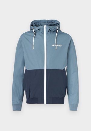 Krāsains viegls džemperis gaiši zilā un tumši zilā krāsā ar baltu rāvējslēdzēju un auklām; elastīgi aproces un apakšmala; logotips krūtīs.