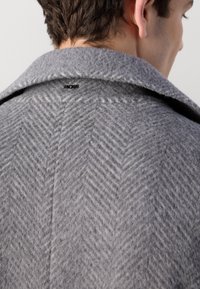 Grå herringbone uldfrakke med bred krave og subtil BOSS-logo på ryggen, der viser en blød, struktureret overflade.
