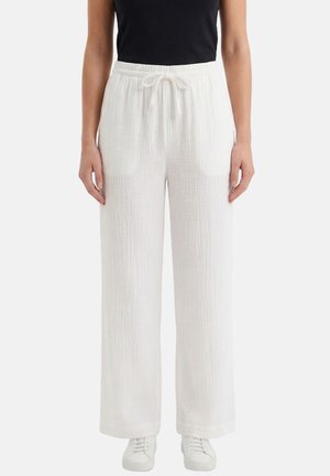 Donna che indossa pantaloni bianchi larghi e strutturati con elastico in vita e coulisse, abbinati a sneaker bianche e top nero senza maniche.