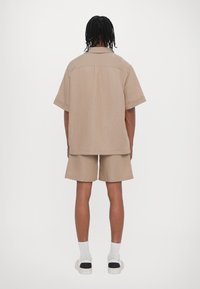 Beige Kurzarmhemd und passende Shorts aus strukturiertem Stoff. Verfügt über einen geraden Schnitt mit Kragen und einer lässigen Silhouette.