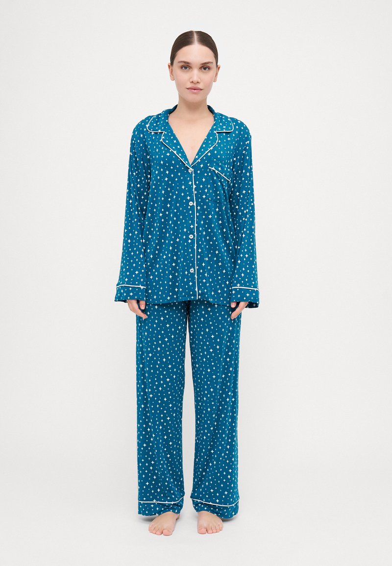 Conjunto de pijama teal com padrões de estrelas brancas, apresentando uma camisa com botões, gola e mangas compridas, e calças largas a condizer.