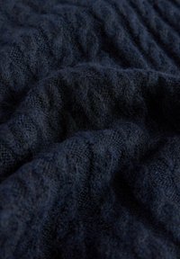 Mørkeblå strikket stof med et struktureret mønster, der har hævede, bølgeagtige former og en blød, fluffy tekstur over hele overfladen.