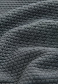 Grijze stoffen met een textuur, voorzien van een gewatteerd patroon van verhoogde diamanten, waarmee een zachte, geweven textuur met een subtiele glans wordt getoond.