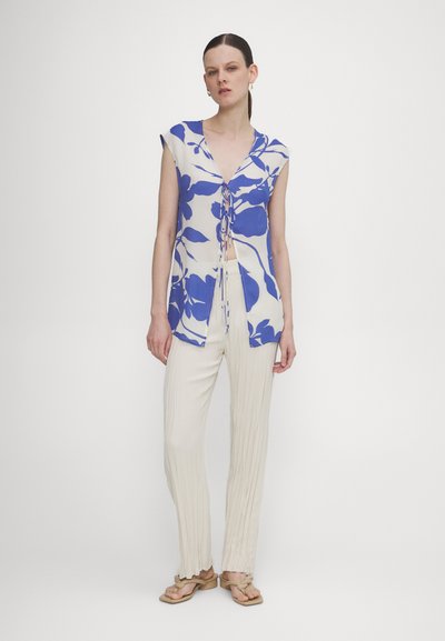 Bloemmotief, blauwe en witte top met korte mouwen en v-hals met strikdetail, gecombineerd met roomkleurige, geplooide, wijde broek.