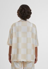 Chemise à manches courtes surdimensionnée à motif carreaux crème et jaune pâle, confectionnée en tissu léger avec une texture douce et une coupe décontractée.