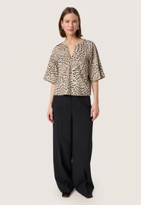 Bluza s uzorkom leoparda, dubokim V-izrezom, kratkim širokim rukavima i strukom koji se prilagođava. Uparena s crnim hlačama širokih nogavica visokog struka.