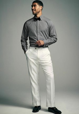 Cămașă gri cu dungi, purtată cu o cravată, pantaloni albi made to measure și mocasini negri, creând un ansamblu formal cu linii curate.