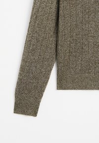 Brun stickad tröja med ribbstruktur, som har långa ärmar och en åtsittande nederkant. Strukturerade linjer skapar ett subtilt mönster.