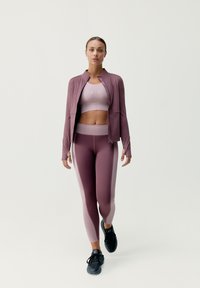 Sportoutfit bestående af en tætsiddende mauve jakke med lynlås, en matchende crop top og leggings med et gradient mauve design, parret med sorte sneakers.
